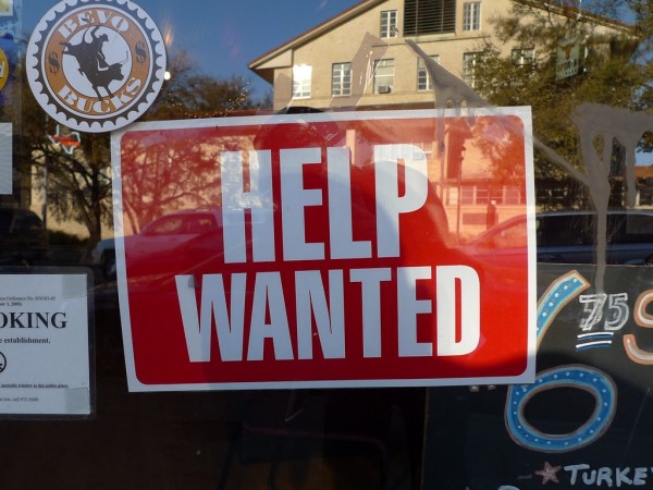 A photo of a retail store with a Now Hiring sign in the window